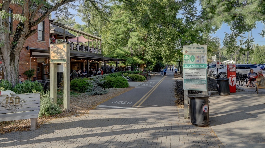 View of a brick building with a restaurant and people dining outside under the trees, beside a pathway for pedestrians, Loveland, Ohio, United States.