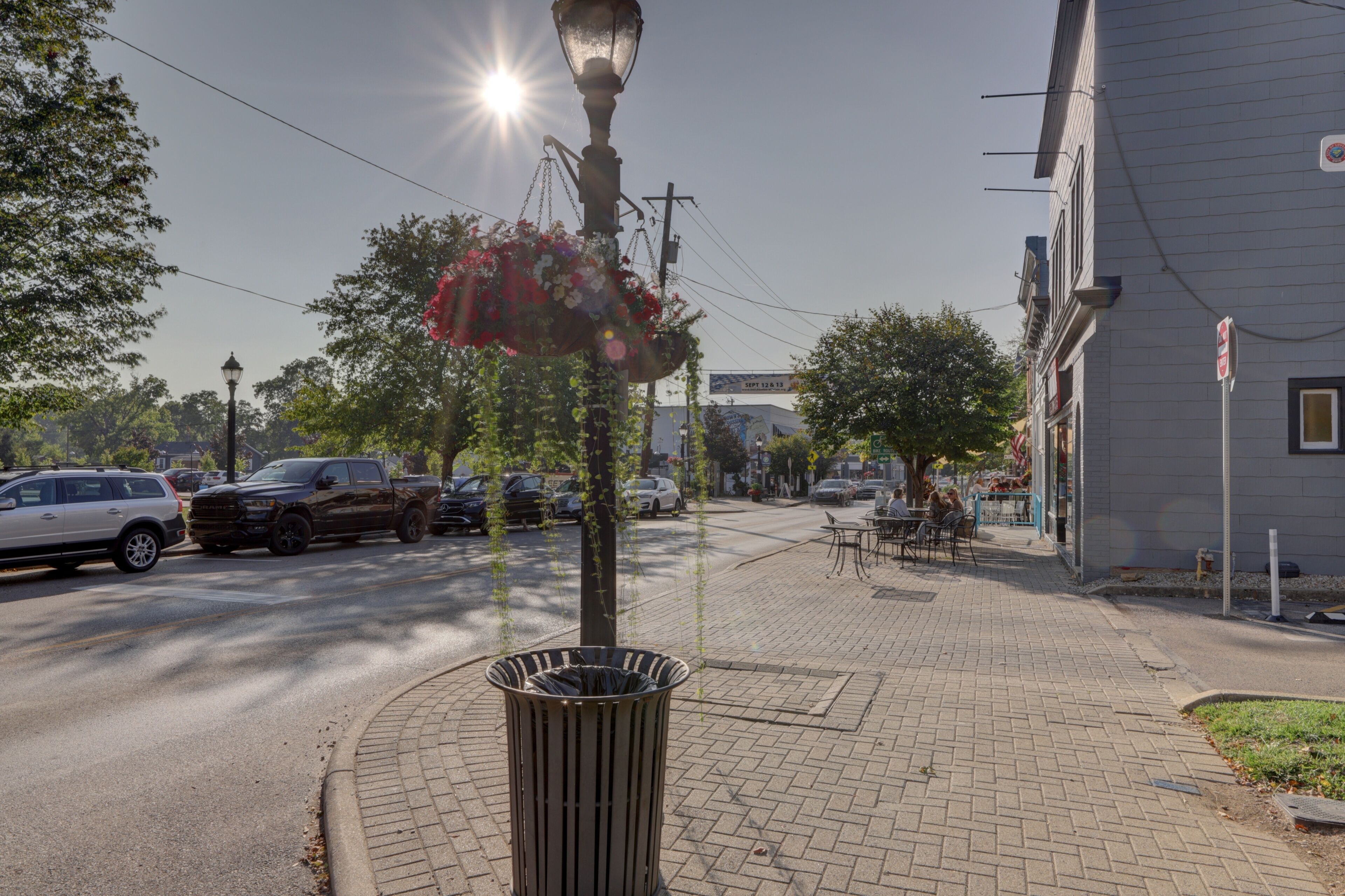 View of the sun casts a warm glow on the brick sidewalk, highlighting the flower basket hanging from an antique lamp post, Loveland, Ohio, United States.