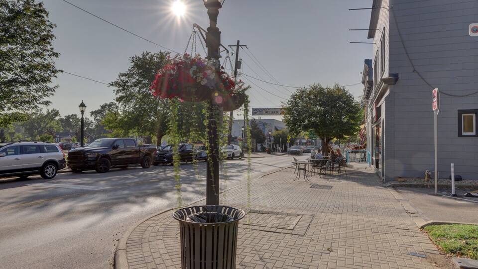 A street with parked cars, a trash can, a hanging flower basket, and a building with a sign.