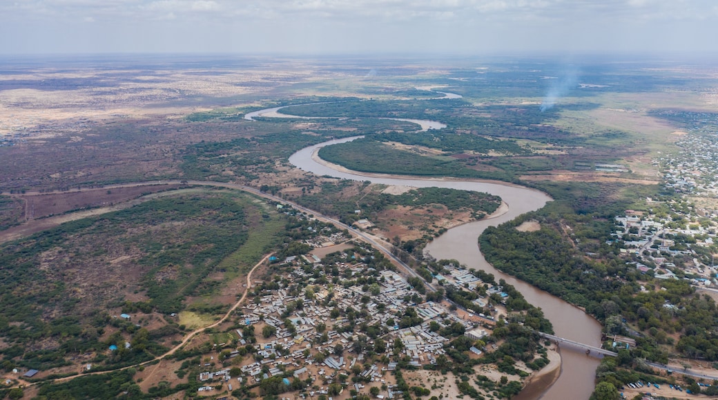Aerial view of Tana river snaking through the dry landscape, the bridge and the town contrasting with the arid surroundings, Garissa, Kenya.