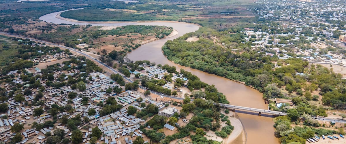 An aerial view of a river winding through a town with a bridge crossing over it.