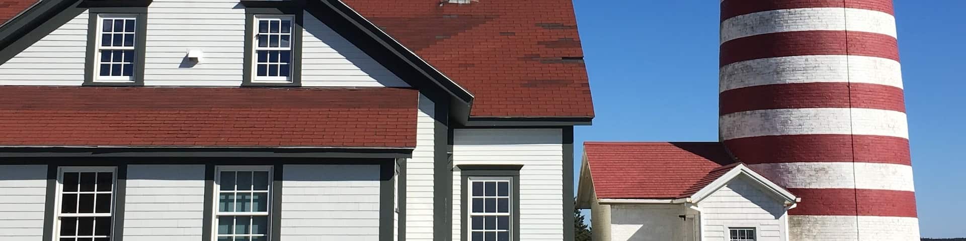 A white house with a red roof and a red and white striped lighthouse.