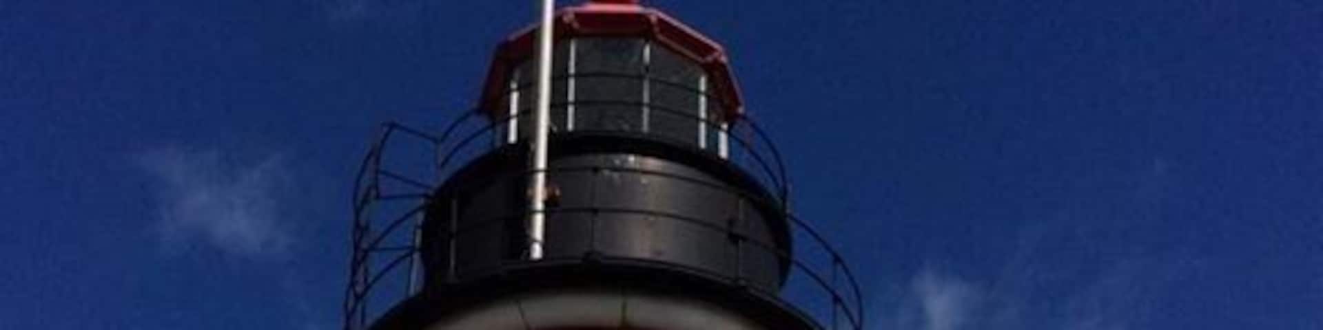 A lighthouse with red and white stripes, a small white building next to it, and a forest in the background.