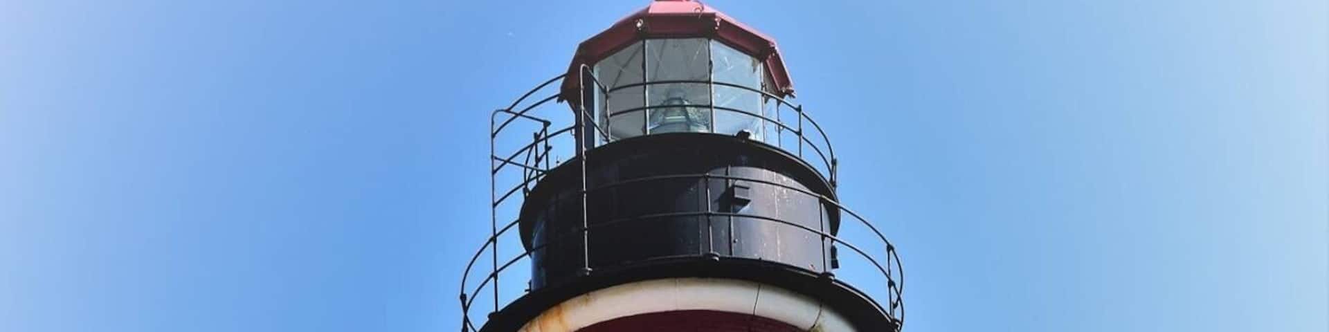 A lighthouse with red and white stripes, a stone marker with text, and a white building with a red roof.