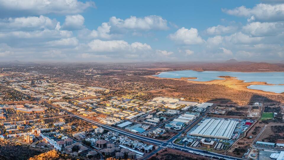 An aerial view of a city with a large body of water, industrial buildings, and surrounding hills.