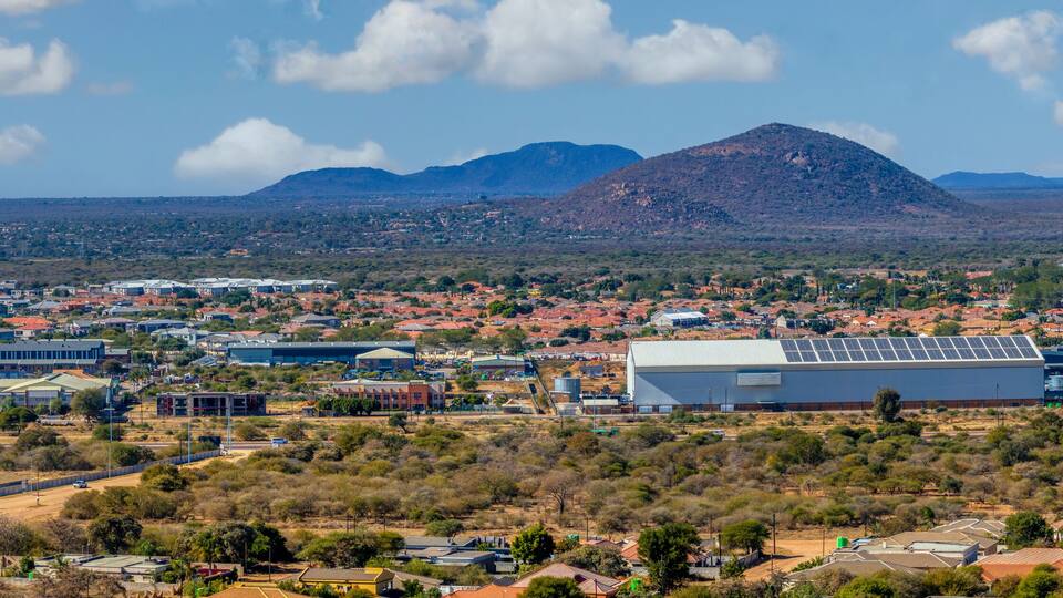 A town with a prominent mountain in the background, surrounded by sparse vegetation and residential buildings.