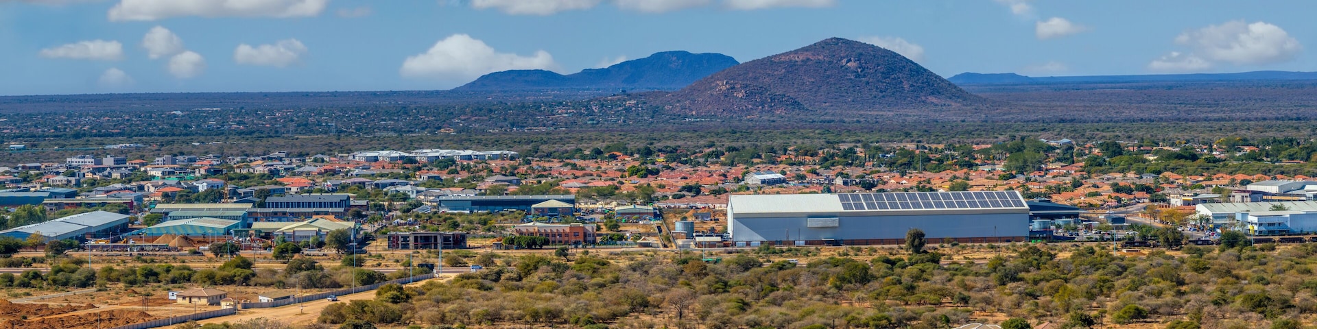 A town with a prominent mountain in the background, surrounded by sparse vegetation and residential buildings.