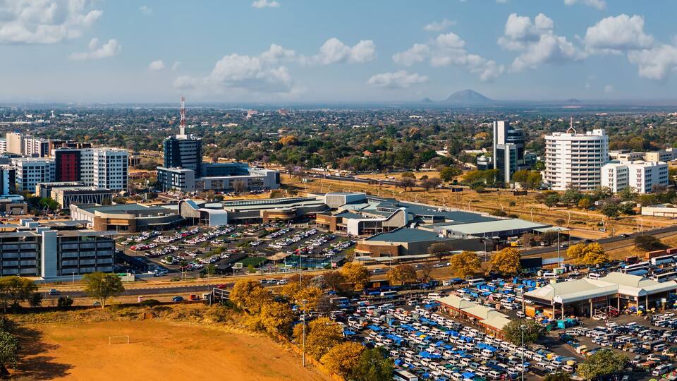 A cityscape with modern buildings, a large parking area, and a distant mountain.