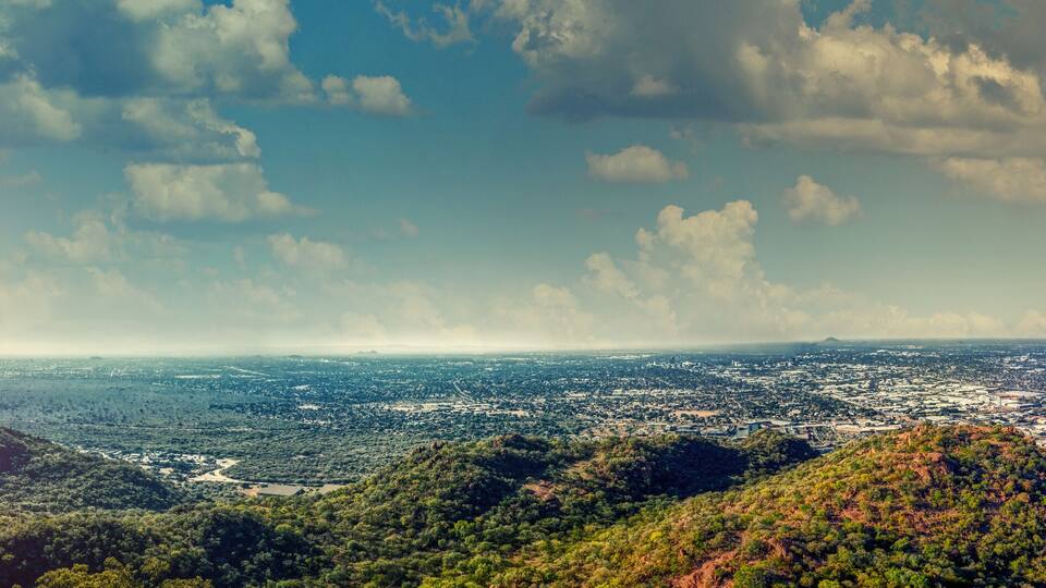 A panoramic view of a city with a river, mountains, and a clear sky.