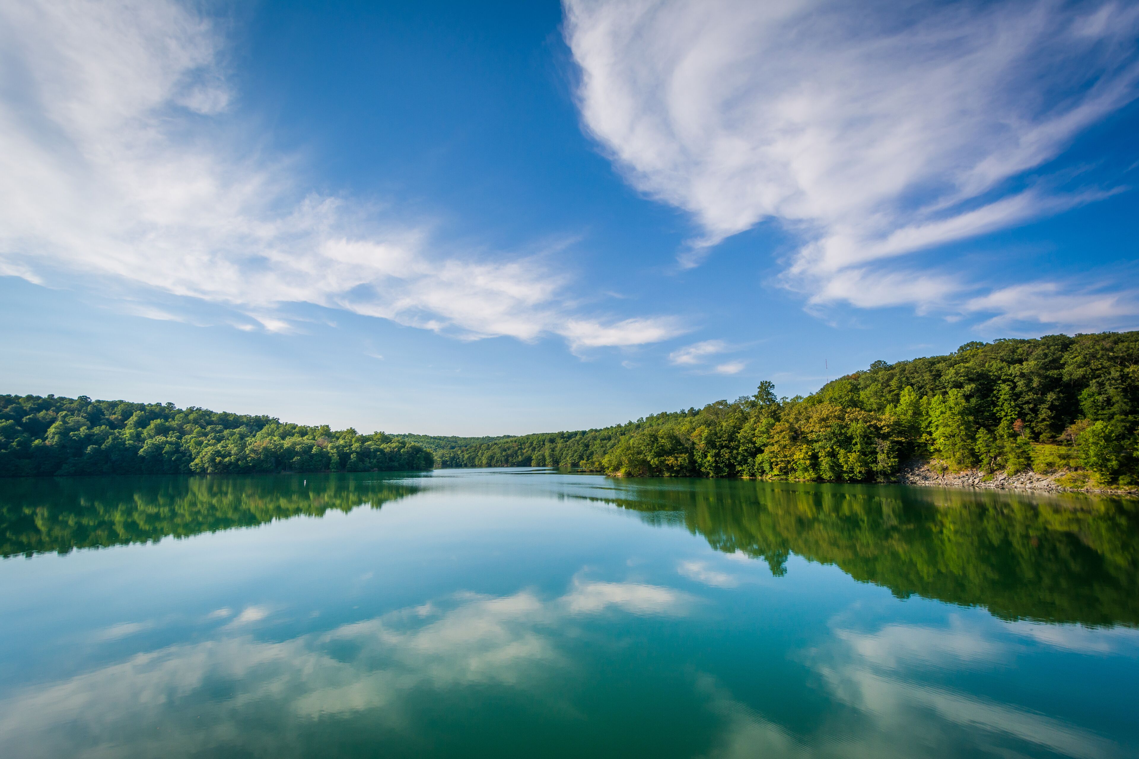 A calm lake reflecting the sky and surrounding forest.