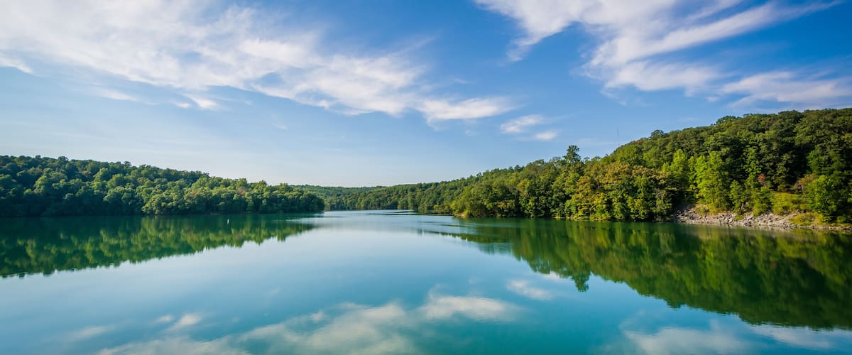 A calm lake reflecting the sky and surrounding forest.
