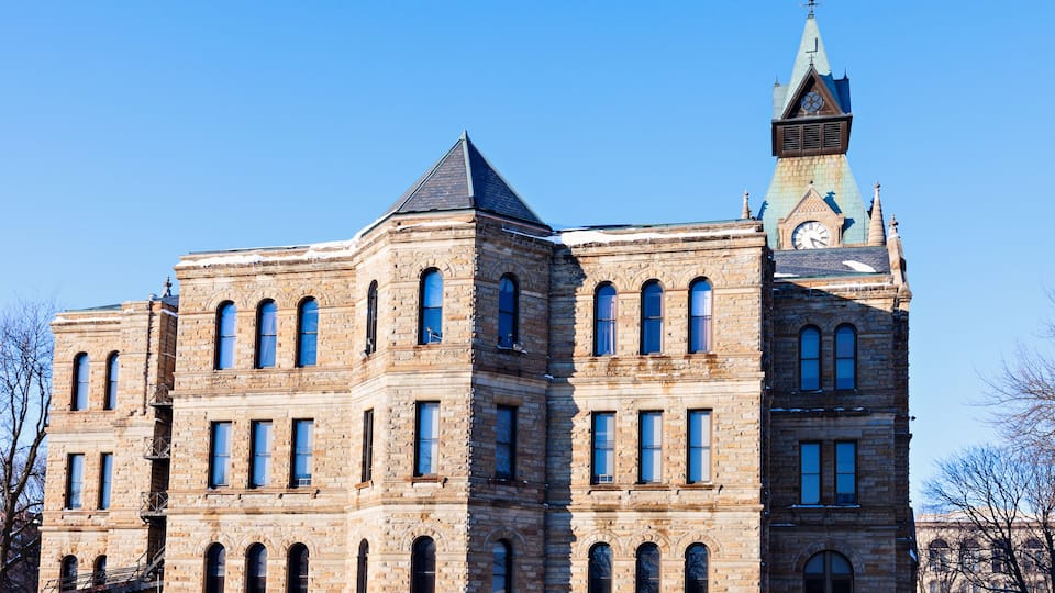A large, historic stone building with multiple arched windows and a prominent tower with a clock.
