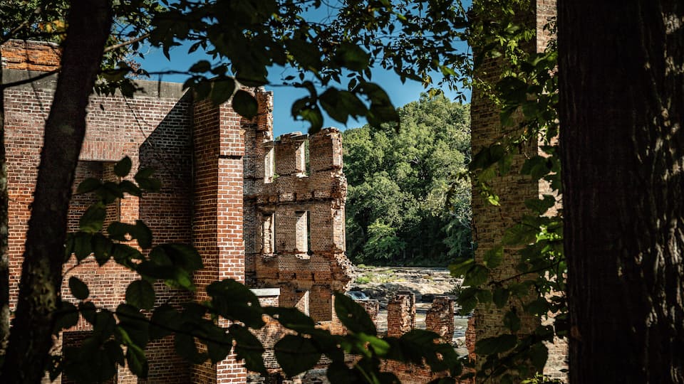 A historic brick building with visible ruins and surrounding trees.