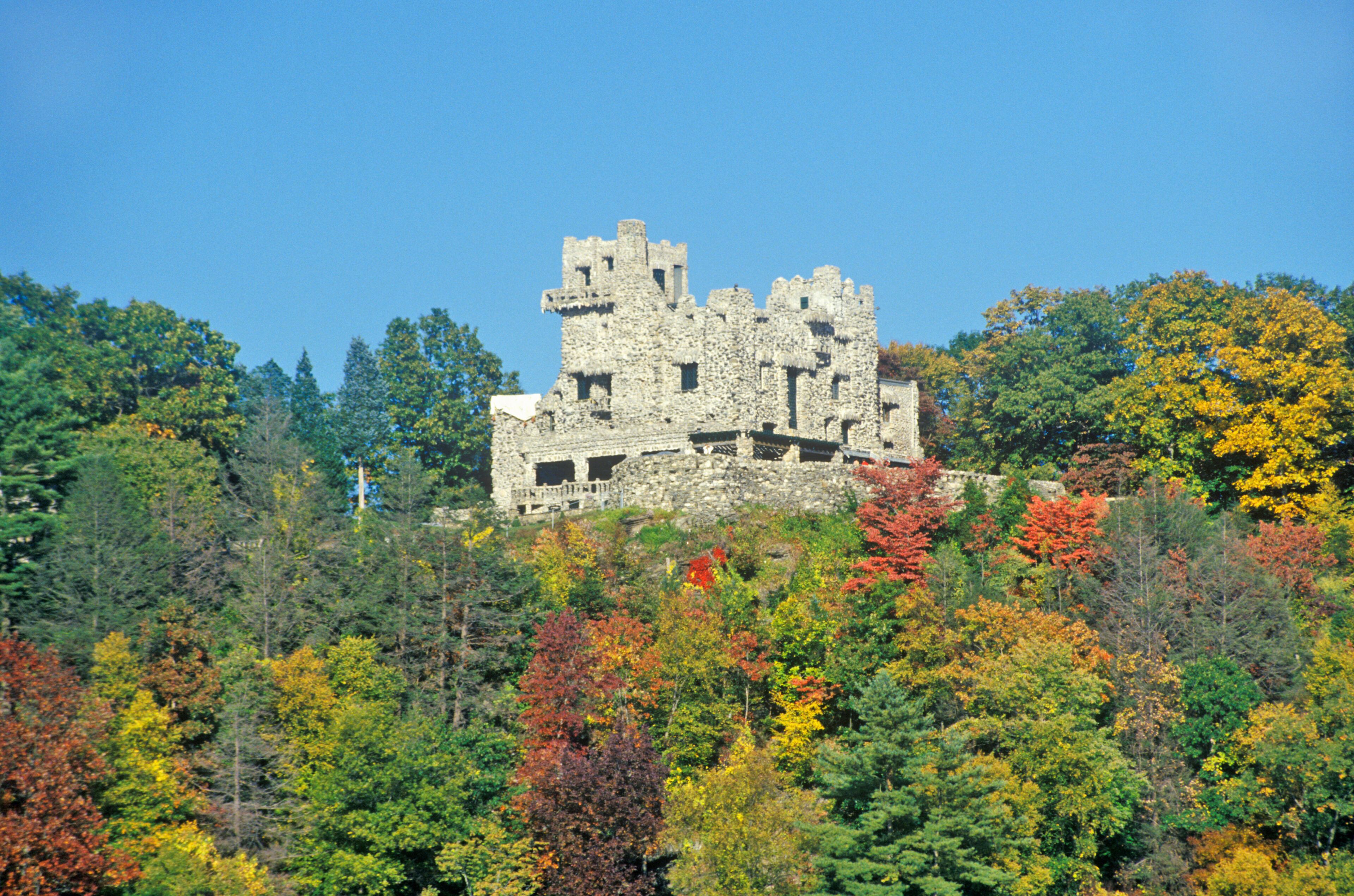 A historic stone castle atop a hill, surrounded by a forest with autumn foliage.