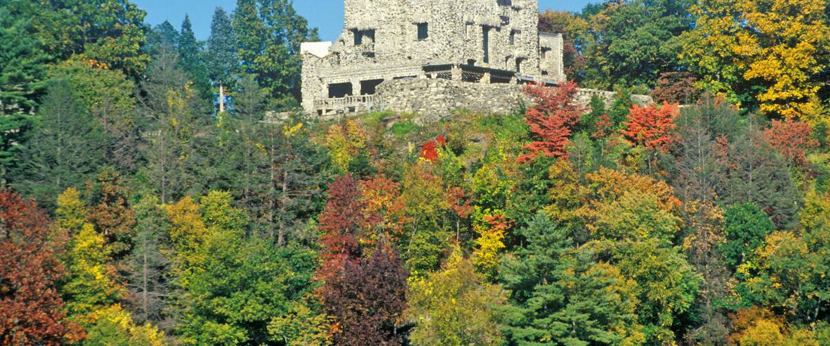 A historic stone castle atop a hill, surrounded by a forest with autumn foliage.