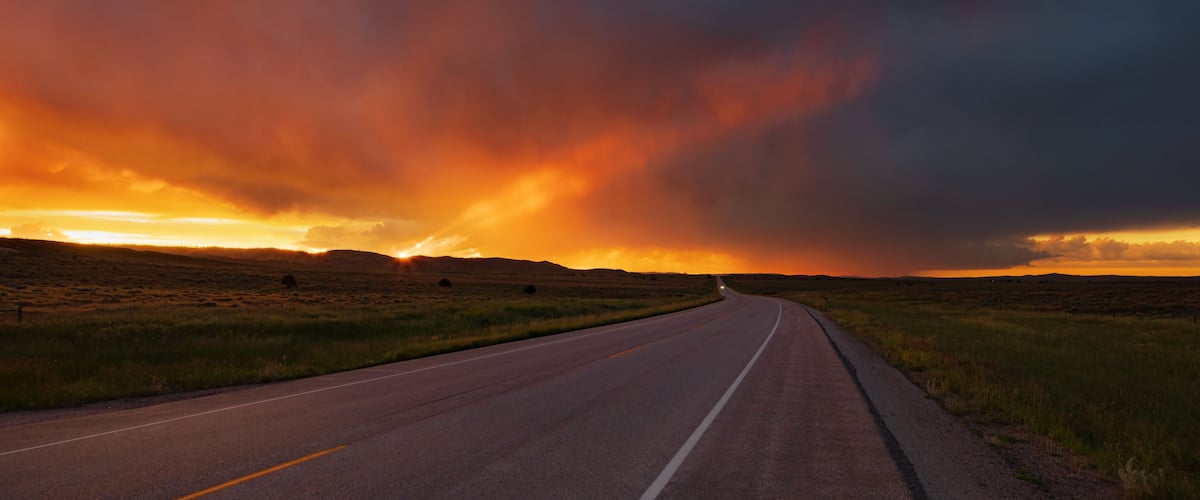 A road curving through a flat landscape under a dramatic sunset sky.