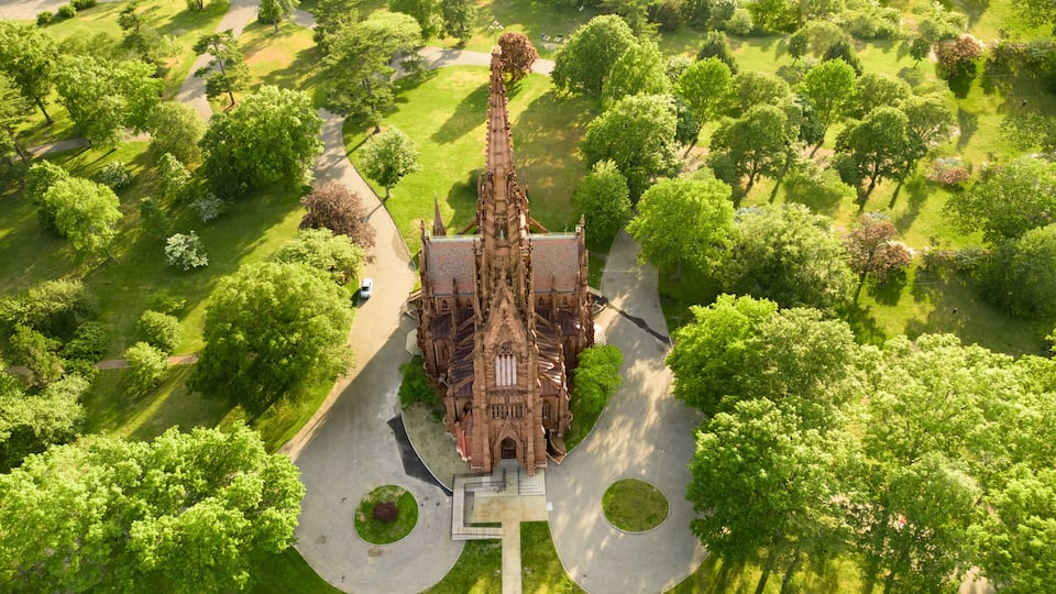 An aerial view of a Gothic-style church surrounded by lush greenery and a winding road.