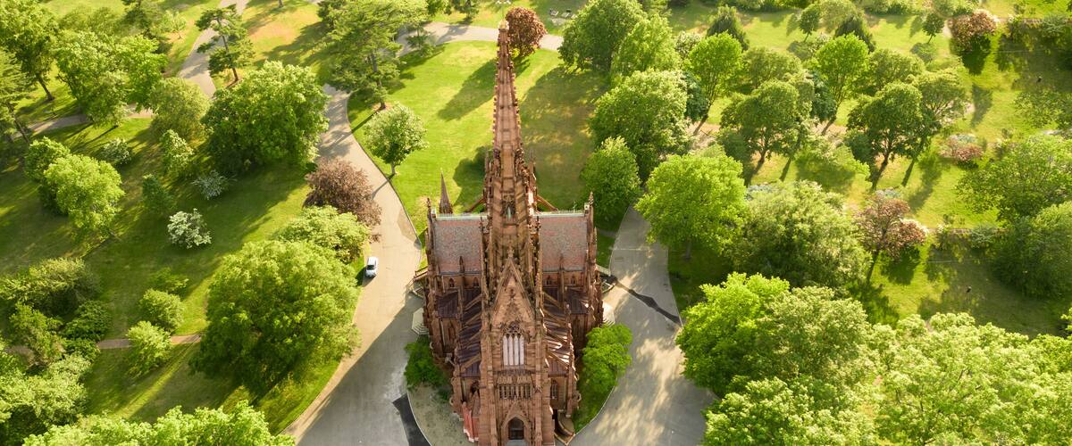 An aerial view of a Gothic-style church surrounded by lush greenery and a winding road.
