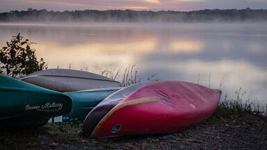 A calm lake at sunrise with three kayaks lined up on the shore.