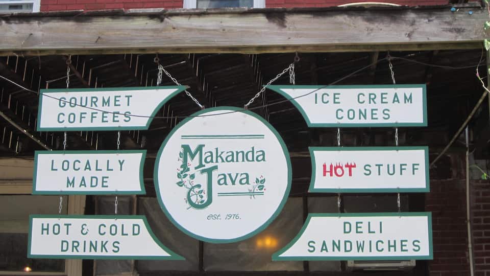 A signboard with various offerings like gourmet coffees, ice cream cones, locally made products, hot and cold drinks, and deli sandwiches.
