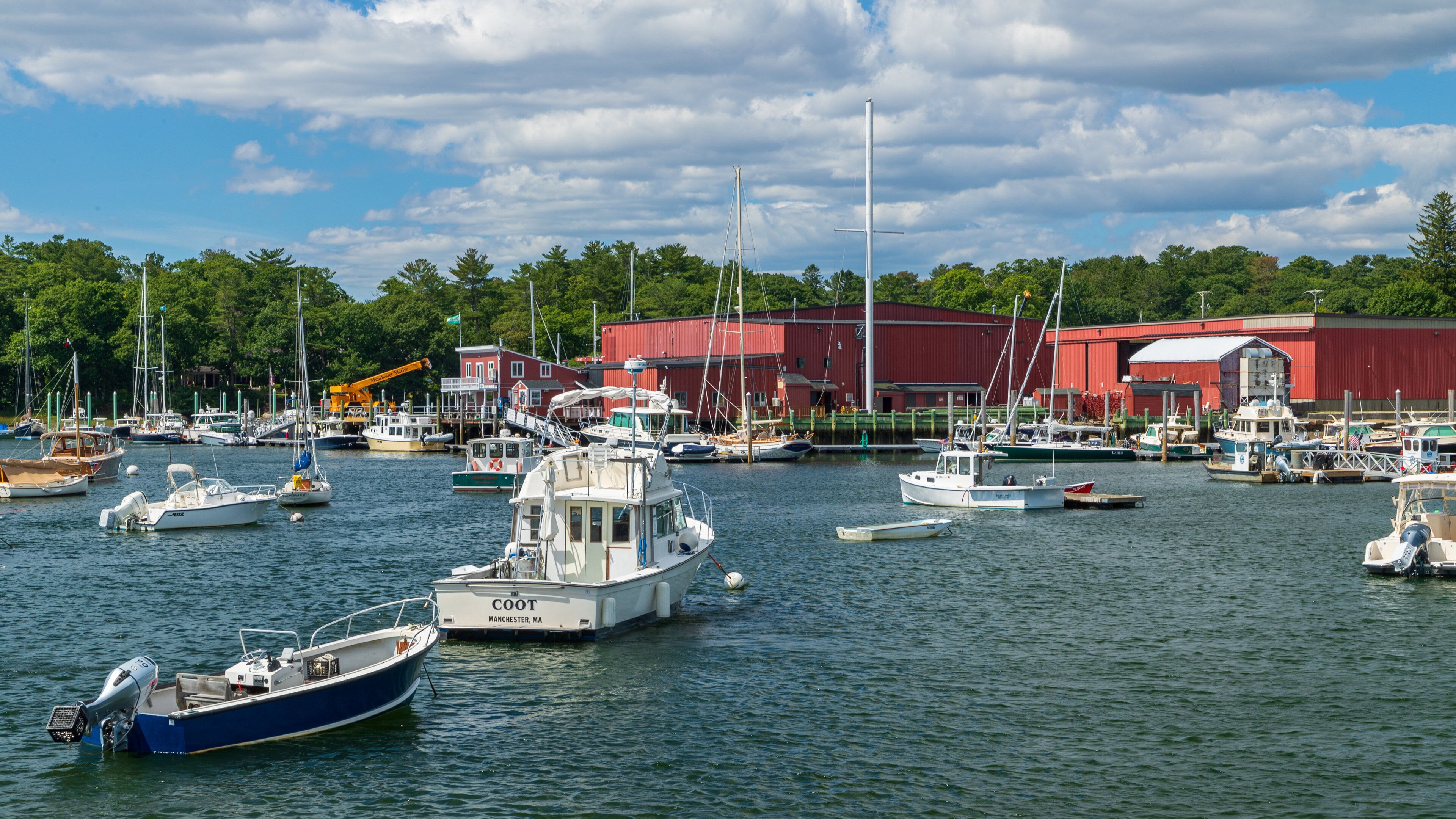 A marina with various boats docked, a red building, and a crane in the background.