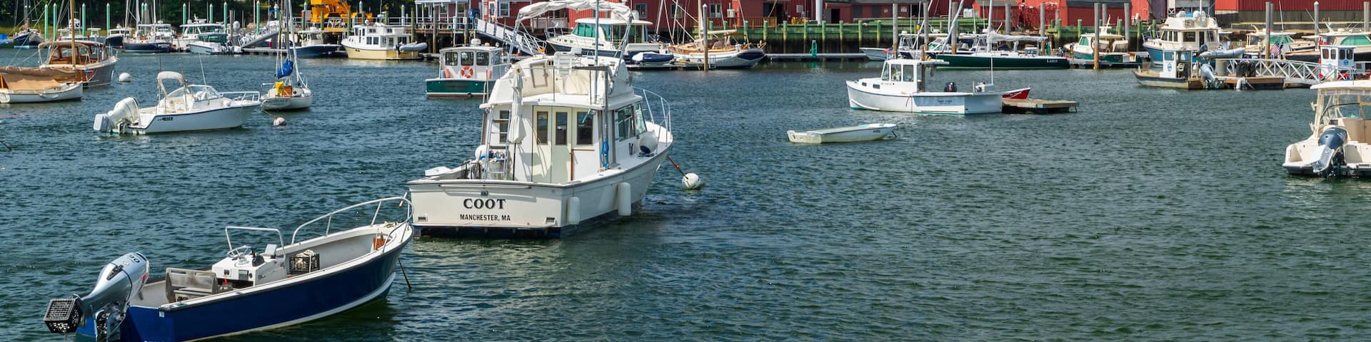 A marina with various boats docked, a red building, and a crane in the background.