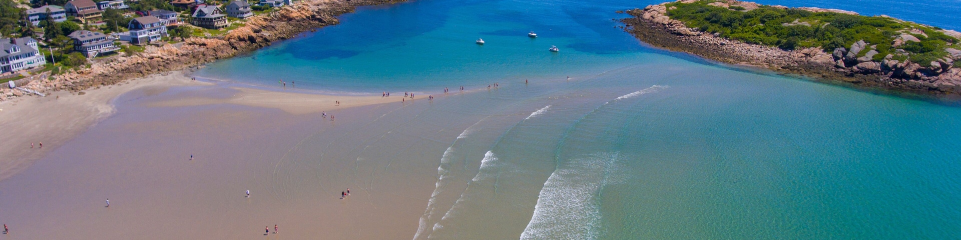 Un pueblo costero con playa, aguas azul turquesa y afloramientos rocosos.
