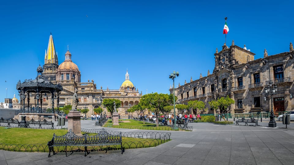 A plaza with a fountain, benches, and a large building with a golden dome.