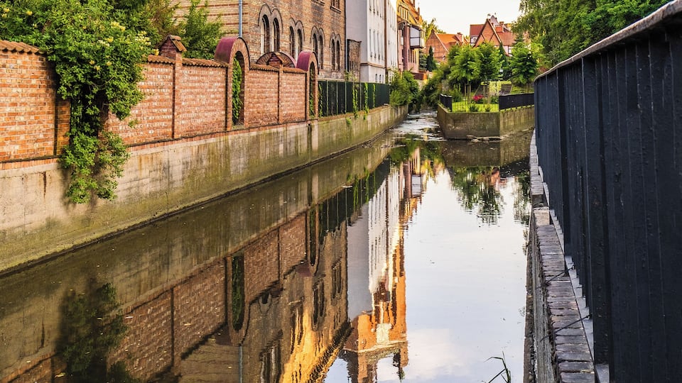 A canal with a brick wall on one side and a building with a tower on the other.