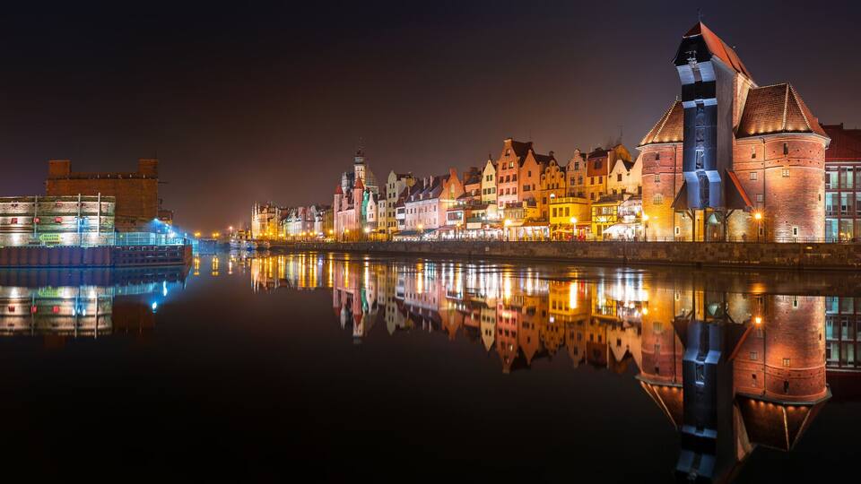 A river with a boat and a row of brightly lit buildings reflecting on the water.