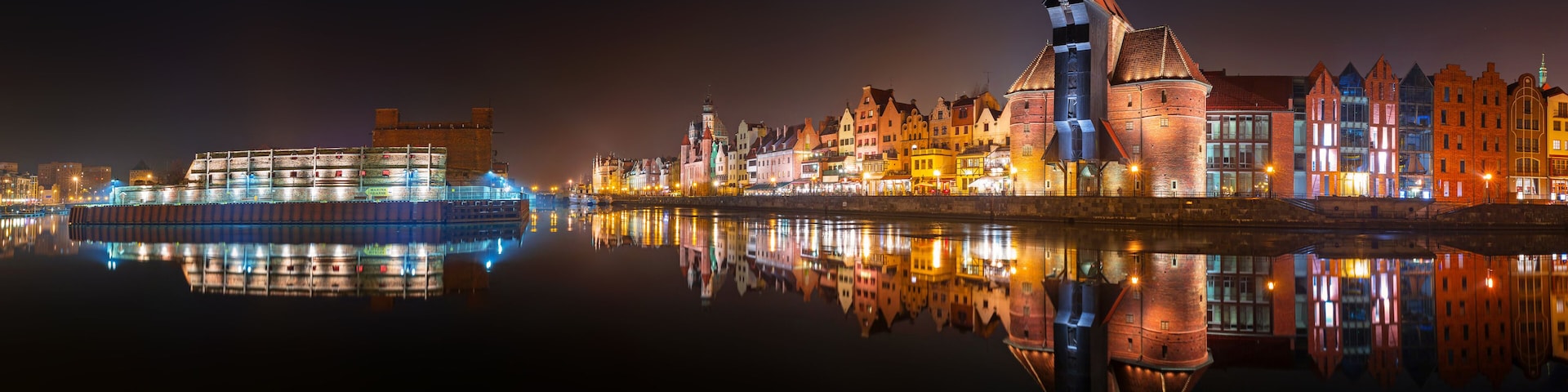 Un río con una barca y una fila de edificios iluminados que se reflejan en el agua.