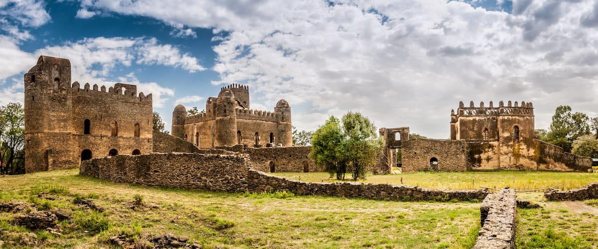 A historic castle with multiple towers and walls, surrounded by grassy fields and trees.