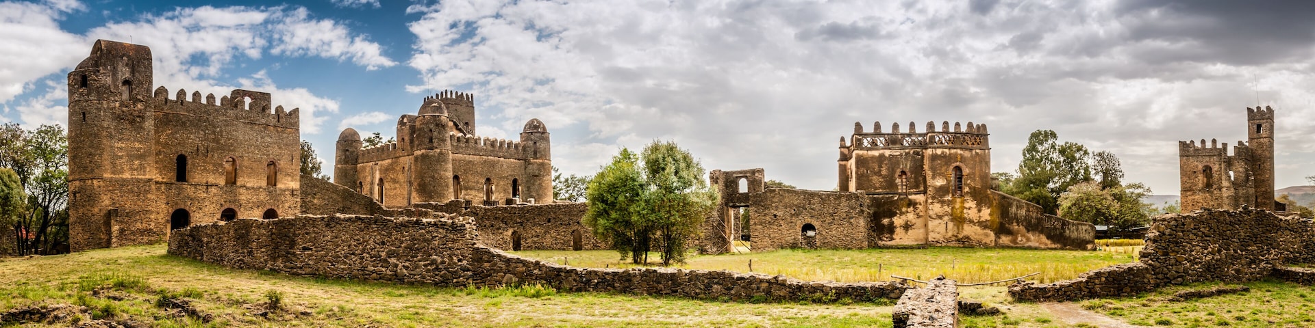 A historic castle with multiple towers and walls, surrounded by grassy fields and trees.