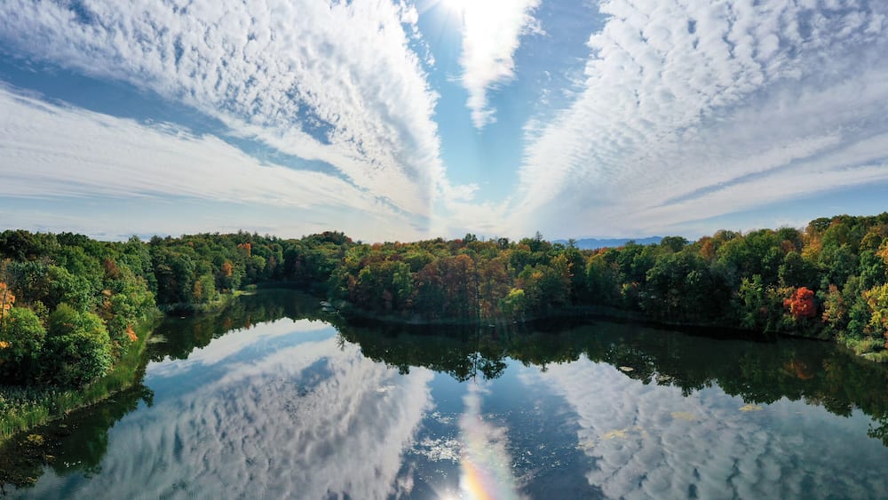 A calm river reflecting the sky and surrounding autumn foliage.