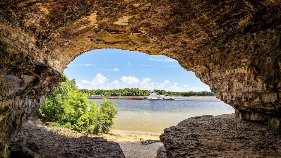 A river with a boat, a sandy beach, and a rocky cave entrance.
