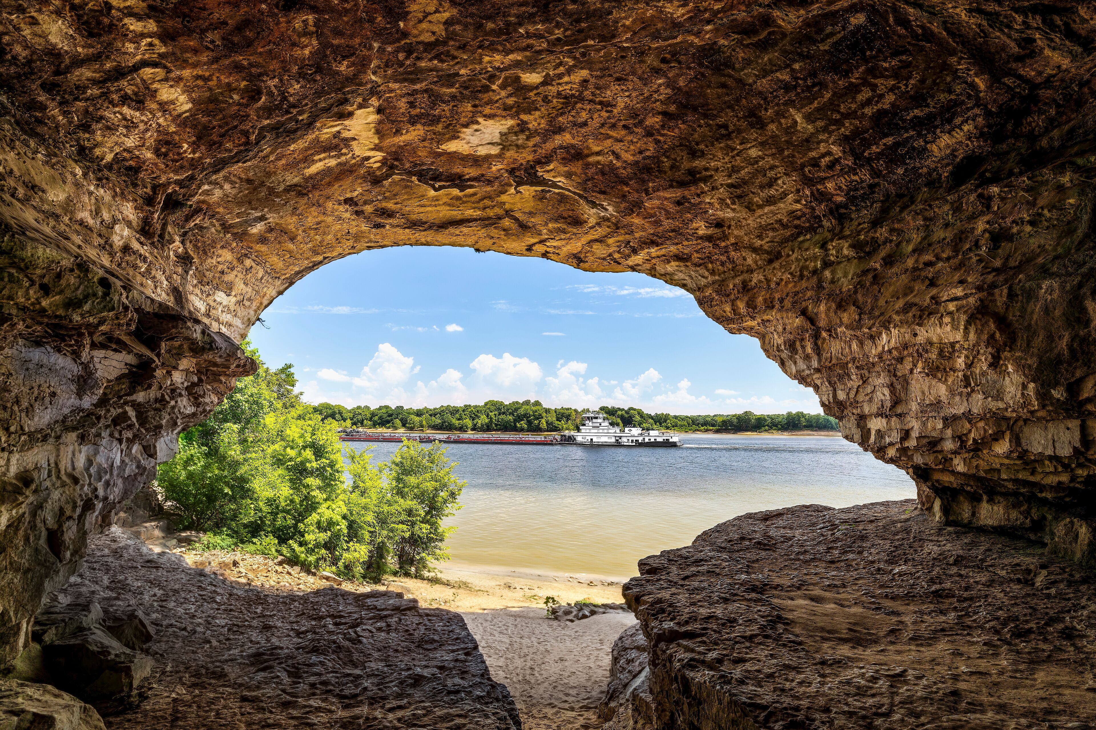 A river with a boat, a sandy beach, and a rocky cave entrance.