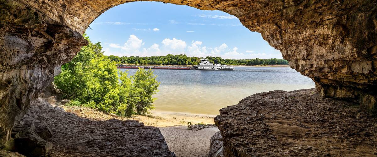 A river with a boat, a sandy beach, and a rocky cave entrance.