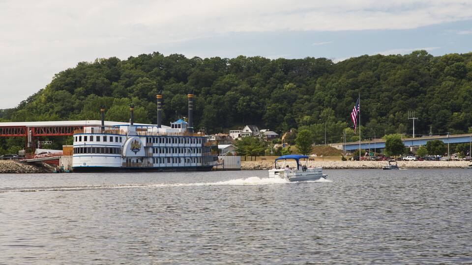 A river with a ferry and a boat, a forested hill, and a bridge.