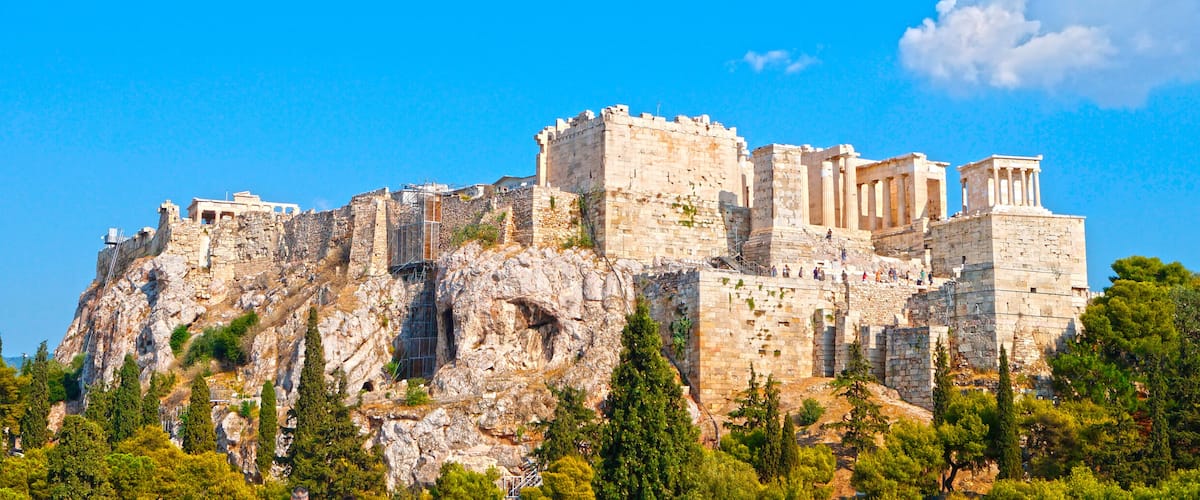 The Acropolis of Athens, featuring ancient ruins, including the Parthenon, on a rocky hill with surrounding greenery.