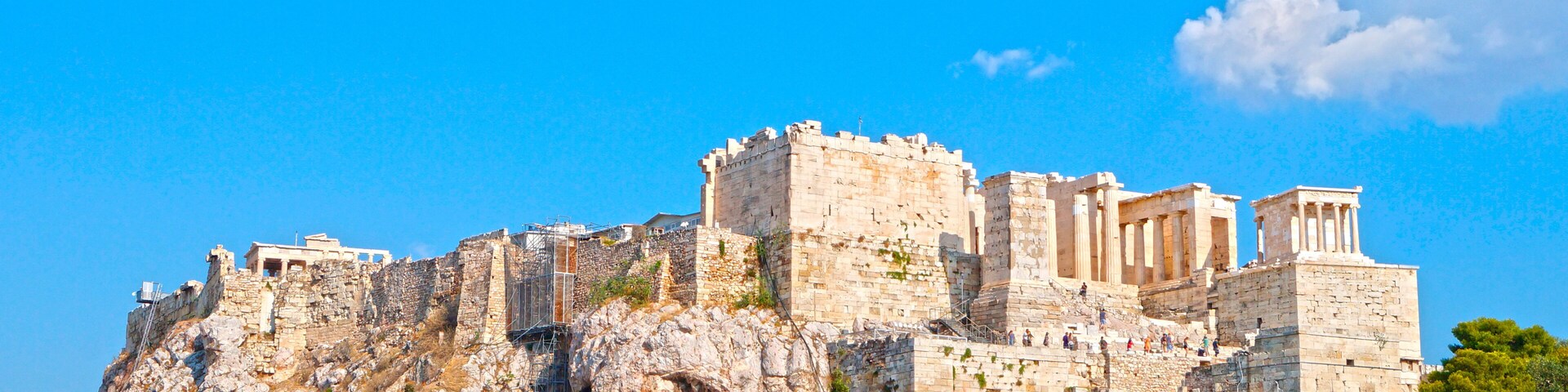 The Acropolis of Athens, featuring ancient ruins, including the Parthenon, on a rocky hill with surrounding greenery.