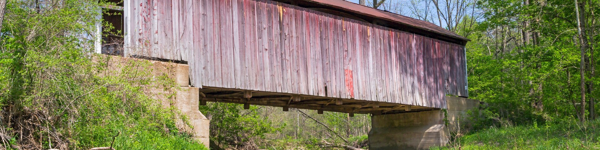Un puente cubierto de madera sobre un arroyo poco profundo rodeado de árboles.