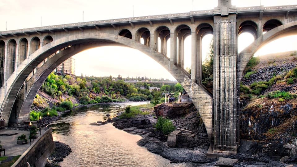 A large stone bridge spanning a river with a rocky riverbank and greenery on the sides.