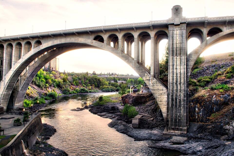 A large stone bridge spanning a river with a rocky riverbank and greenery on the sides.