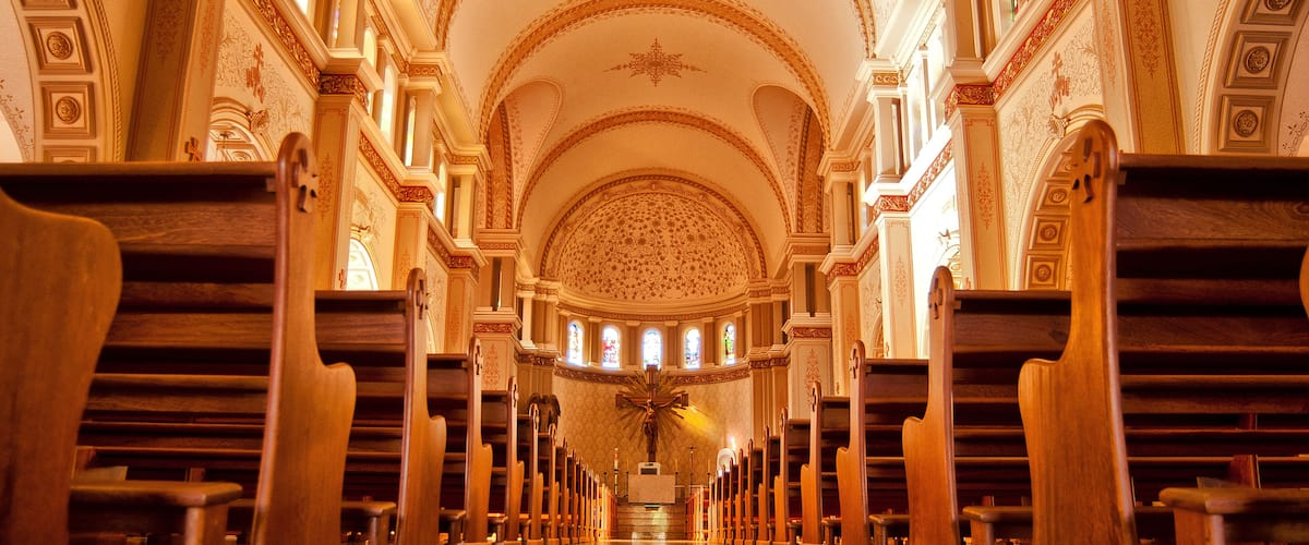 A church interior with ornate architecture, wooden pews, and a central altar.
