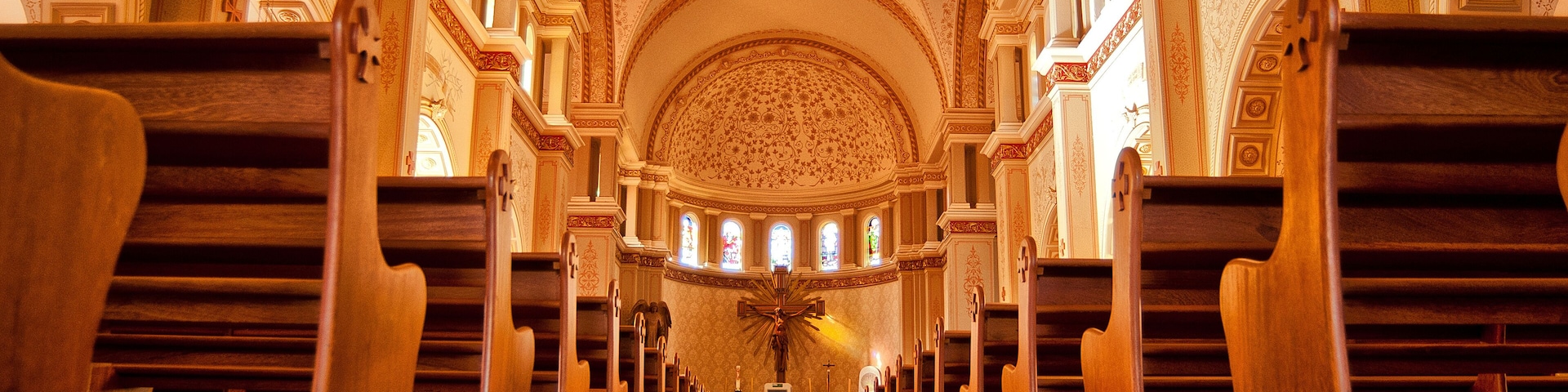 A church interior with ornate architecture, wooden pews, and a central altar.