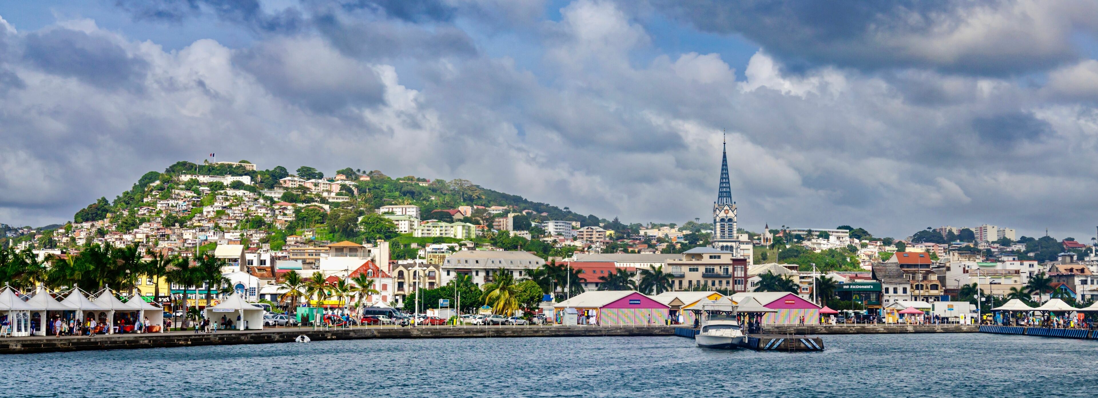 A coastal cityscape with a prominent church spire, a marina with boats, and colorful buildings along the waterfront.