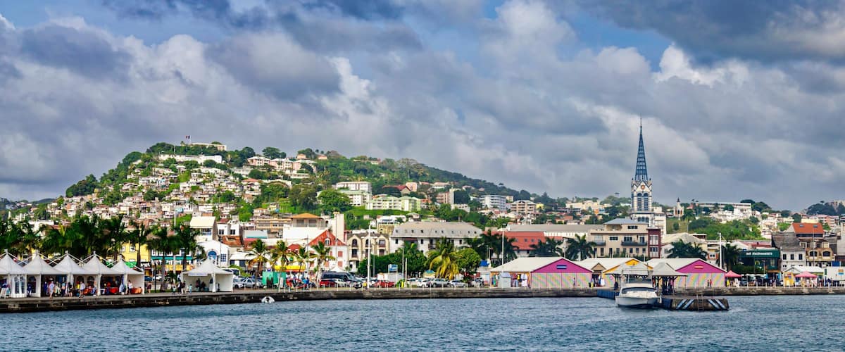 A coastal cityscape with a prominent church spire, a marina with boats, and colorful buildings along the waterfront.