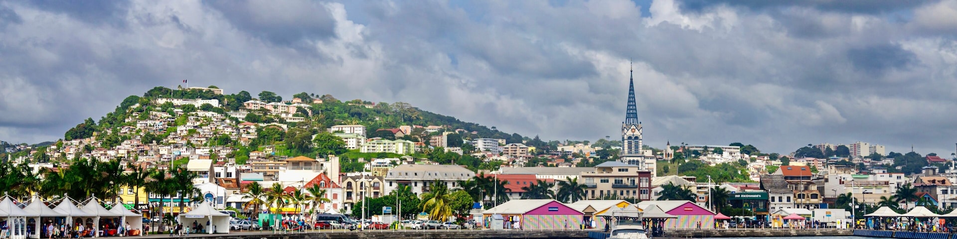 A coastal cityscape with a prominent church spire, a marina with boats, and colorful buildings along the waterfront.
