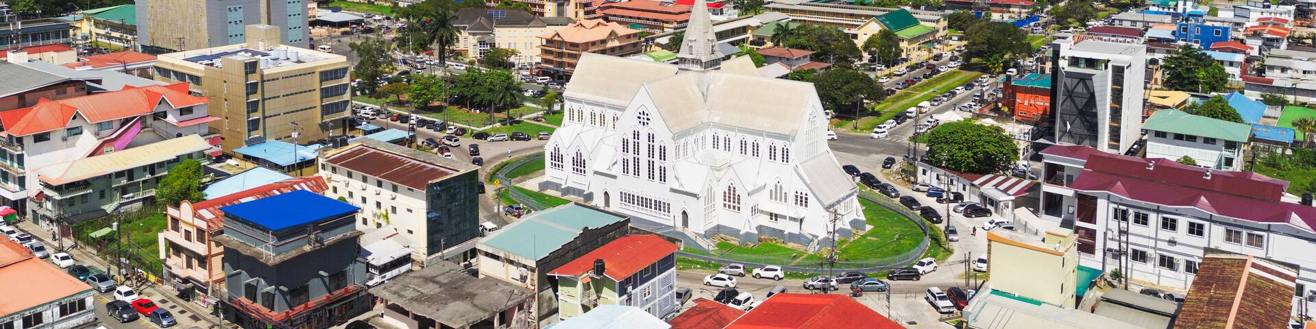Aerial photo of Georgetown, Guyana, with colorful colonial architecture, St. George’s Cathedral, bustling streets, and a waterfront along the Demerara River