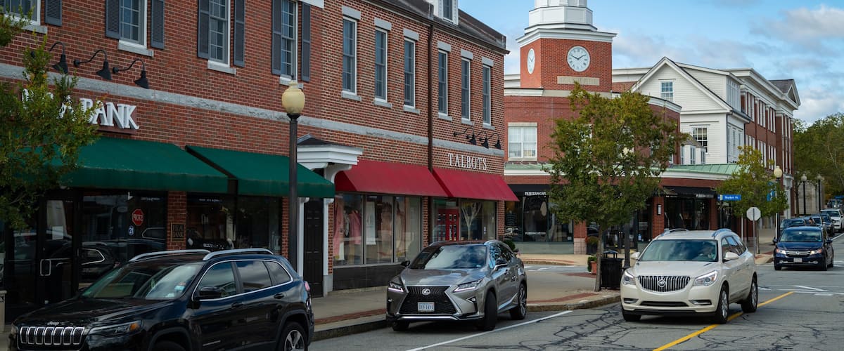A street with brick buildings, a clock tower, and parked cars.